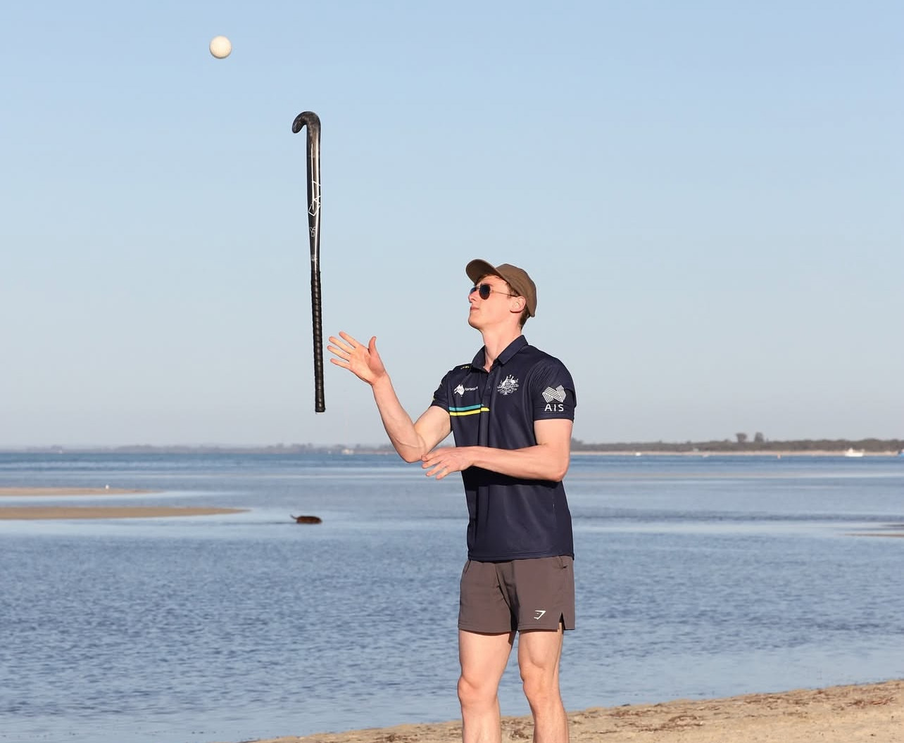 stick-flip-hockey-beach-sunglasses Hockey player flipping stick with ball in mid-air on a sunny beach while wearing sunglasses