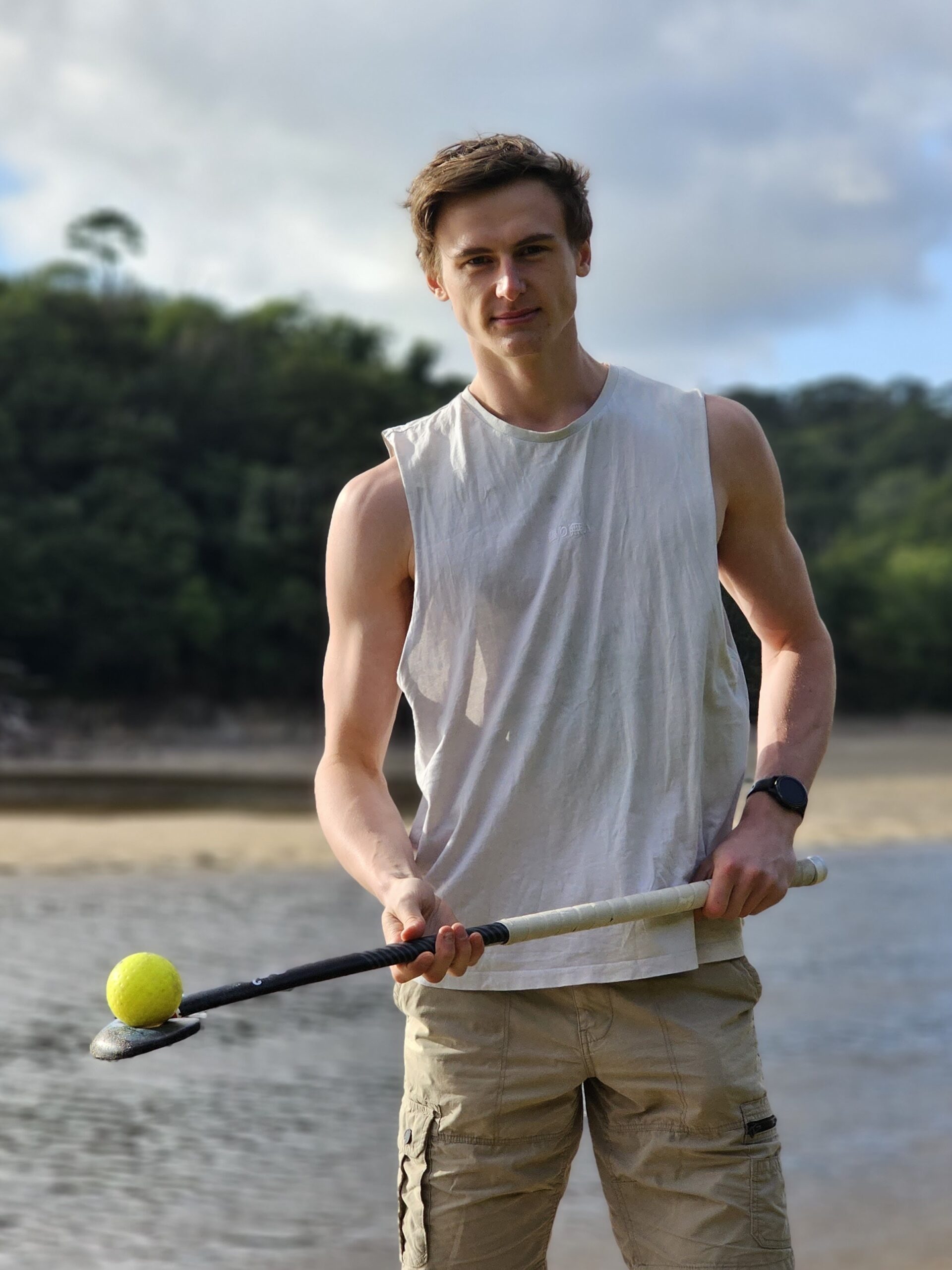 coach-balancing-ball-stick-summer.jpg Hockey coach holding stick with ball balanced on the back in the sun, wearing tank top and shorts