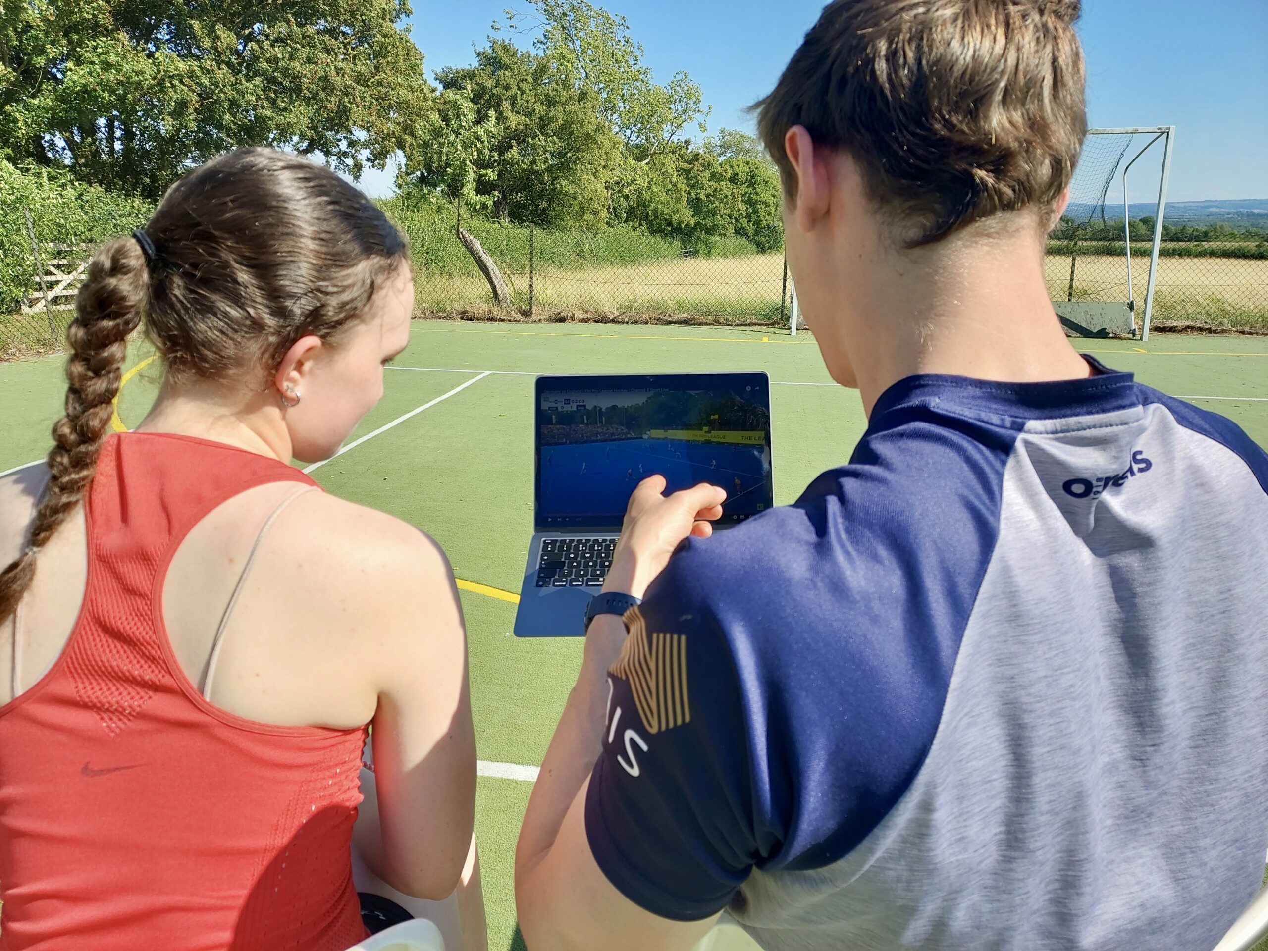 Hockey video analysis session – coach and player Hockey coach and player reviewing match footage together on a laptop during a video analysis session on the pitch